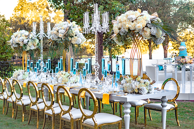 white table, gold clear back chairs, candelabras, tall centerpieces, flowers, wedding tables