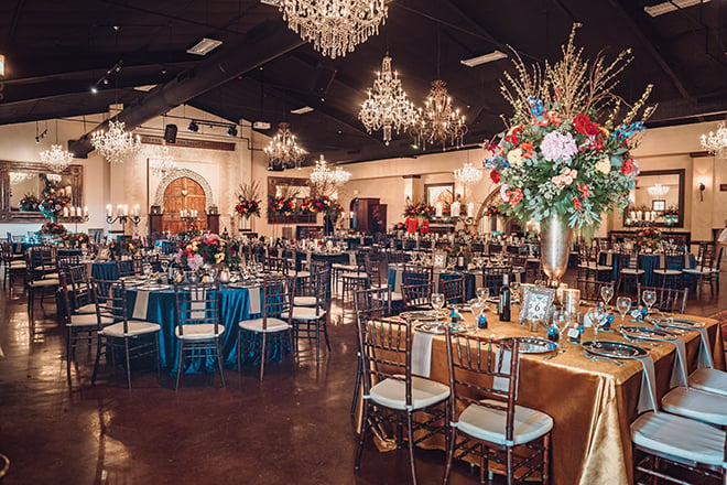 reception decor, madera estates, blue linens, spanish-inspired wedding, chandeliers, candle centerpieces, greenery, table setting, wedding table, gold linens, floral centerpieces 