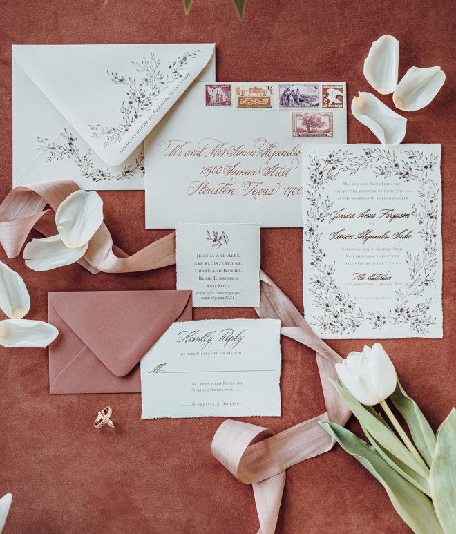Invitation suite on top of dark mauve background with blush ribbons and floral accents 