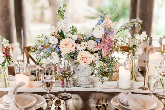 Detail shot of rustic chic table scape underneath an outdoor pavilion at Camp Lucy with a lush pastel colored floral centerpiece, white block candles and robins egg blue tapered candles and elegant place settings 