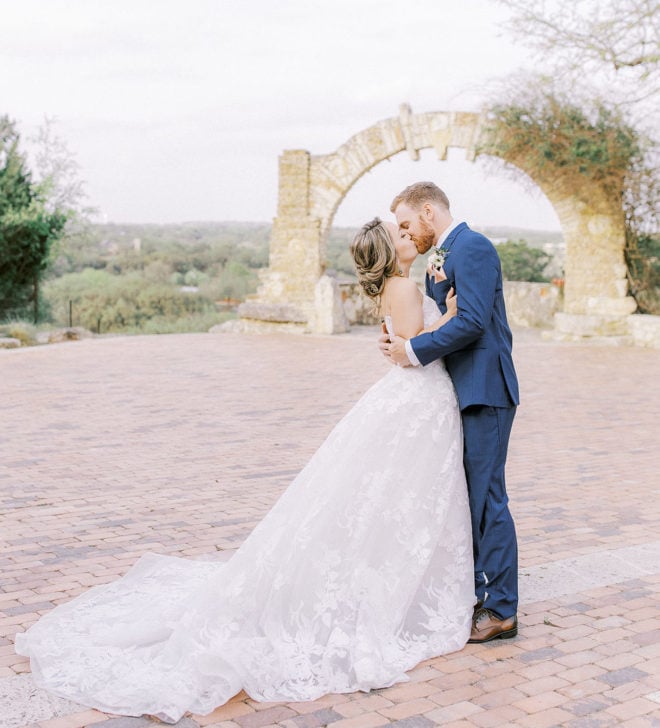 Side profile of bride and groom kissing outside on the grand patio at Camp Lucy with expansive views of the Texas Hill Country 