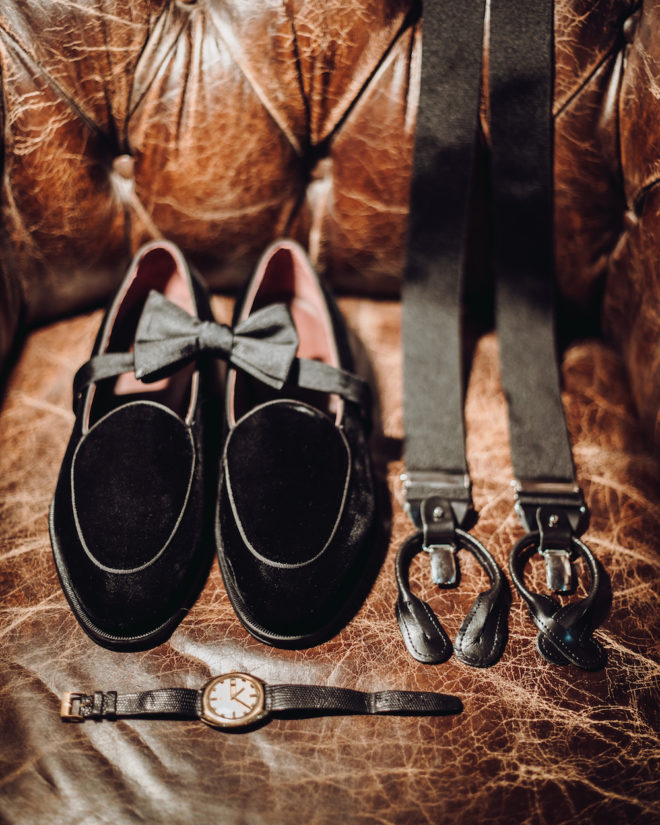 velvet loafers on worn chesterfield sofa leather, vintage watch with black straps, and black suspenders