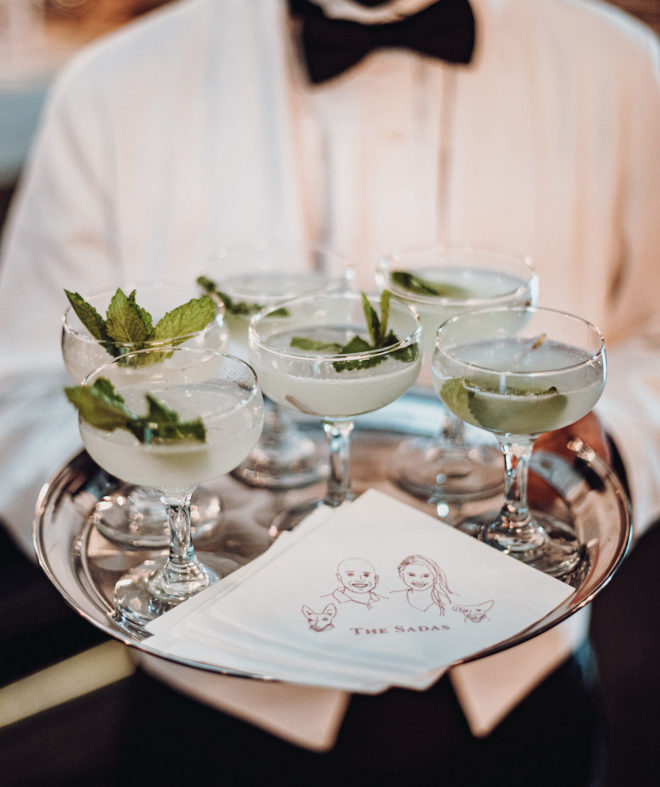 Jackson and Company banquet server holding tray of mint garnished craft cocktails and custom napkins made in the likeness of the bride and groom and their two pet dogs