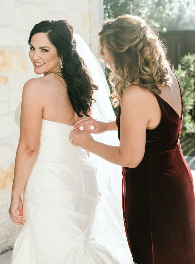 Mom helping bride get dressed in strapless white gown on wedding day. 