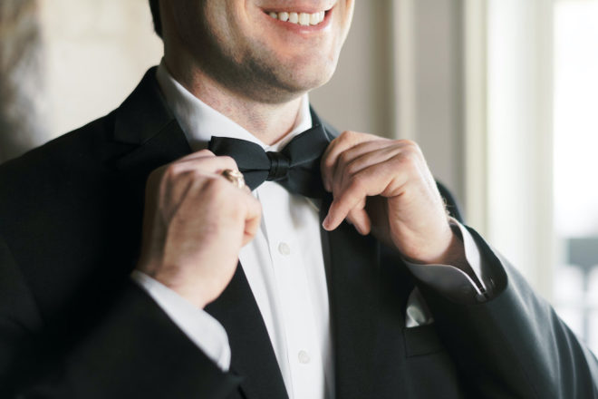 Man adjusts bowtie to get ready for wedding. 