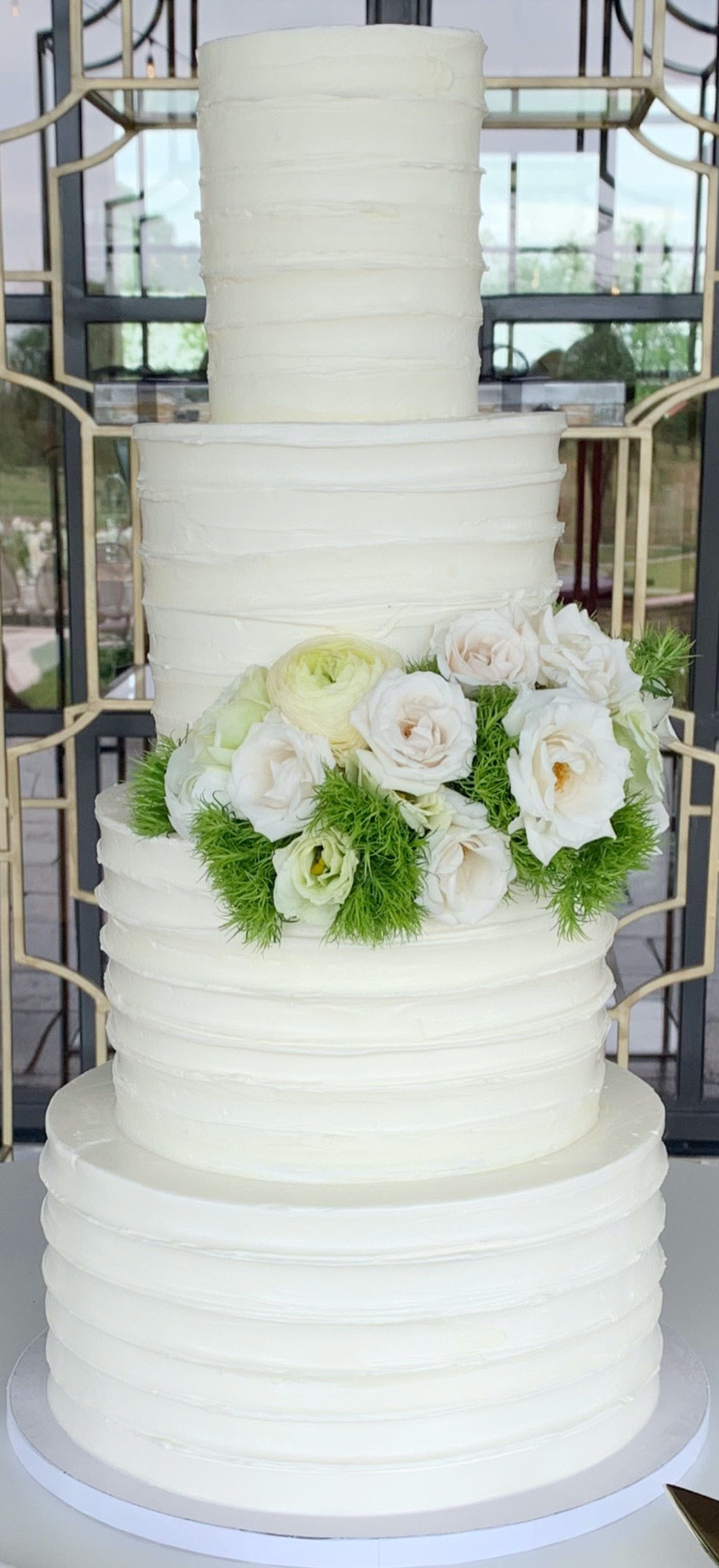 Simple four tier white cake with cream florals and greenery on second tier.