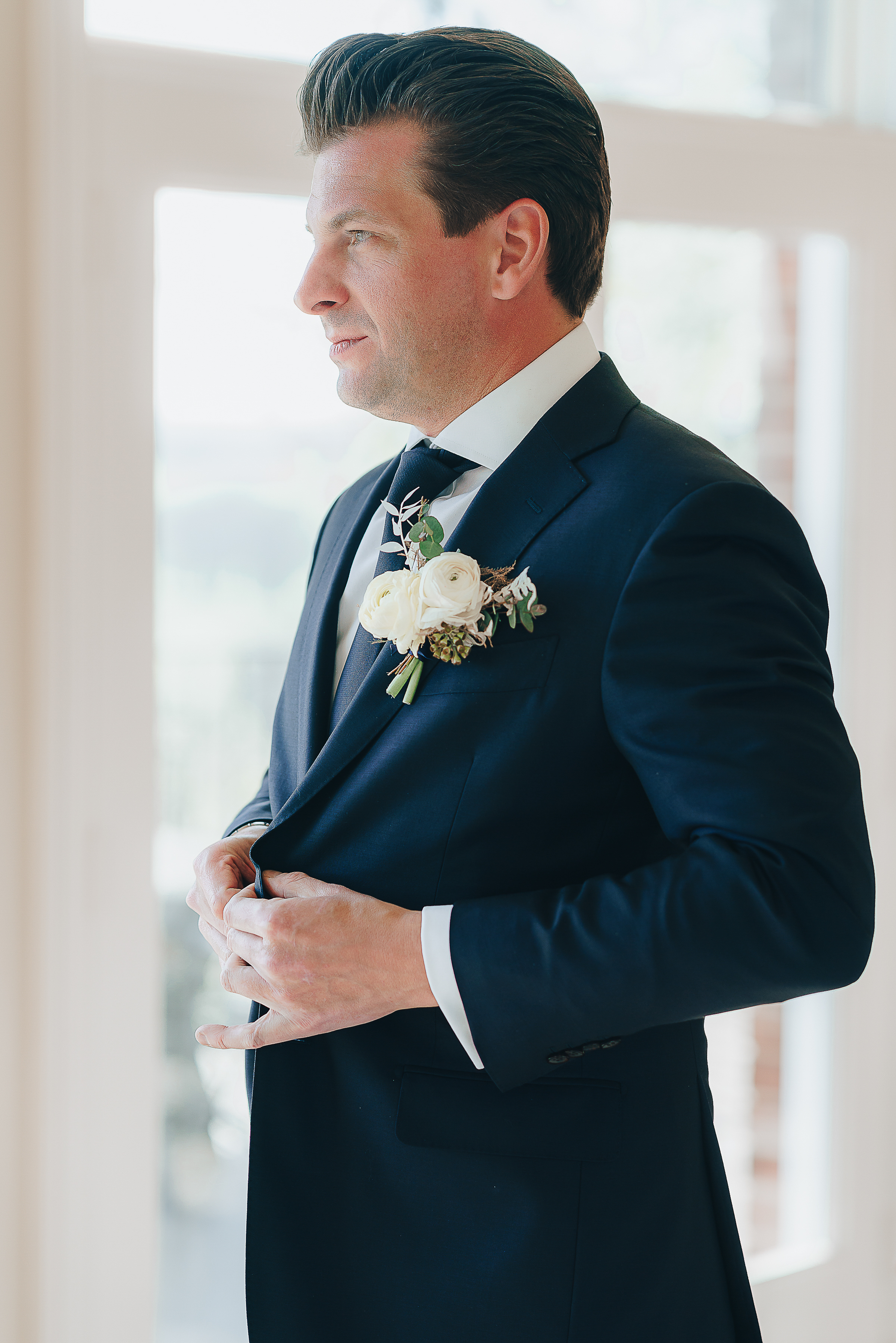 Groom buttoning his suit jacket.