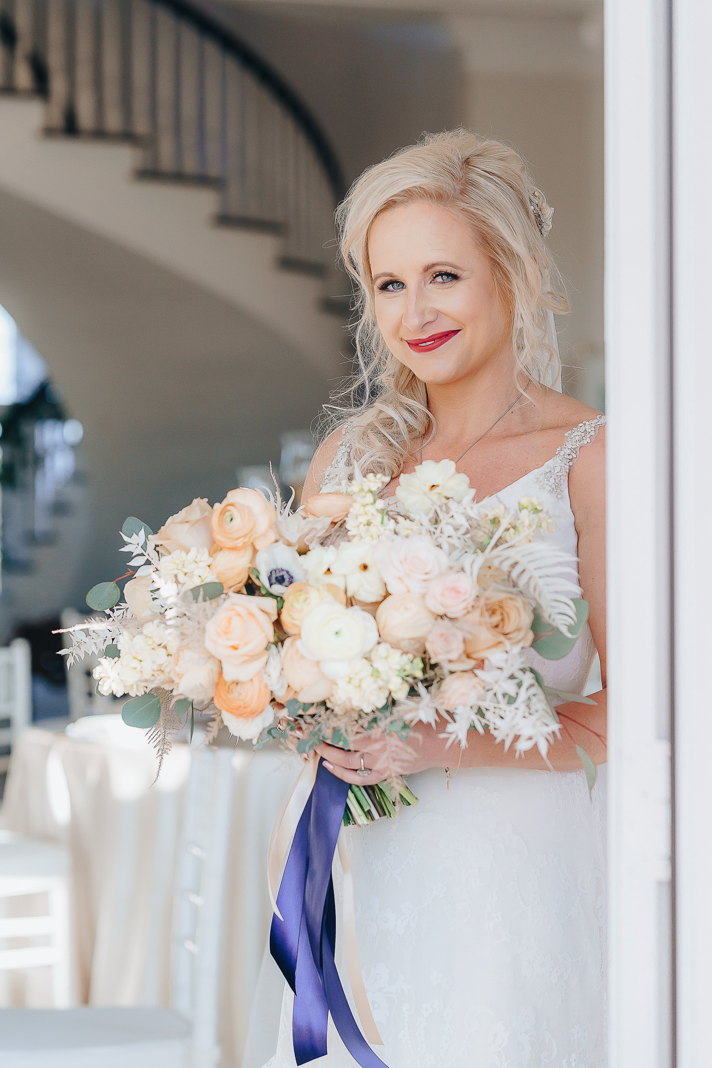 Bride holding a bouquet of blush, peach and white flowers tied by a navy ribbon.