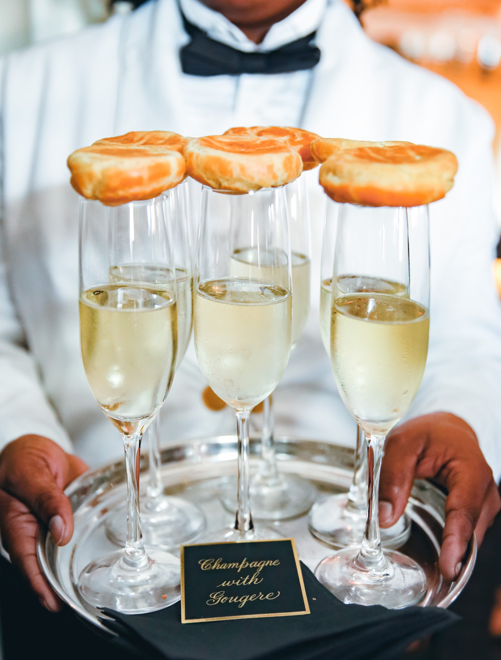  A waiter holds a silver tray with glasses of champagne topped with gougère for the wedding toasts.