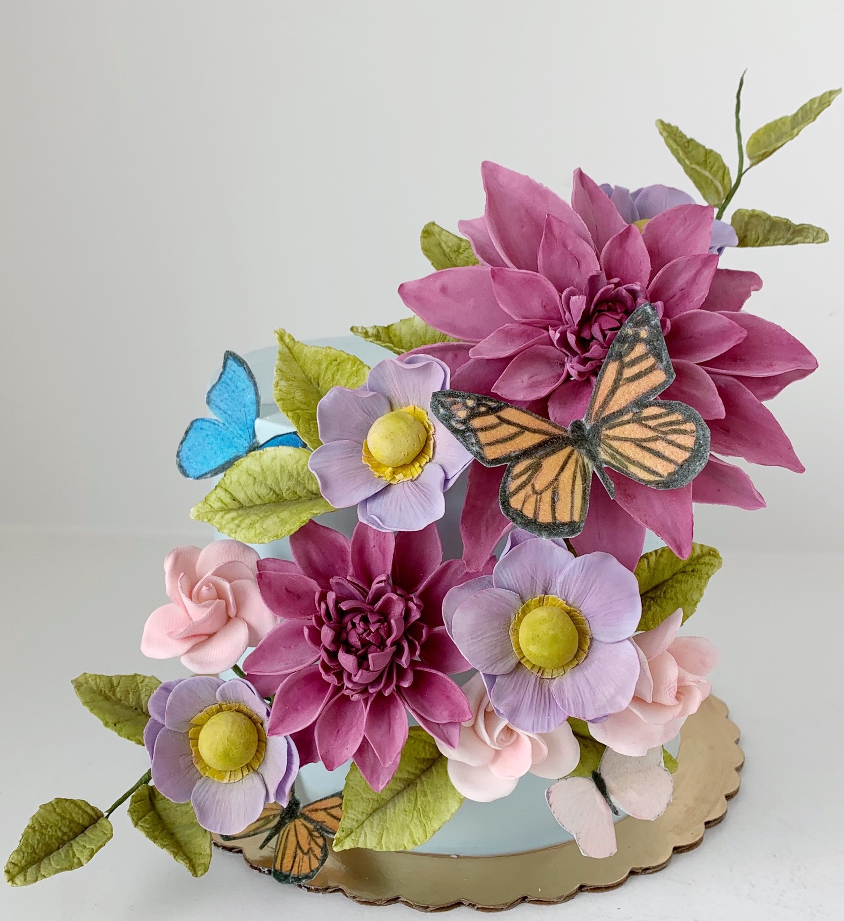 Baby blue mini cake with large purple, fuschia and blush flowers and crepe paper monarch and blue butterflies.