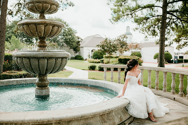 A bride sits on the edge of a tiered stone fountain on the grounds of Bentwater Yacht and Country Club wedding venue.