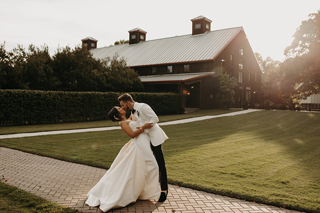 A bride and groom kiss as the sun sets behind The Carriage House wedding venue in Conroe, Texas.