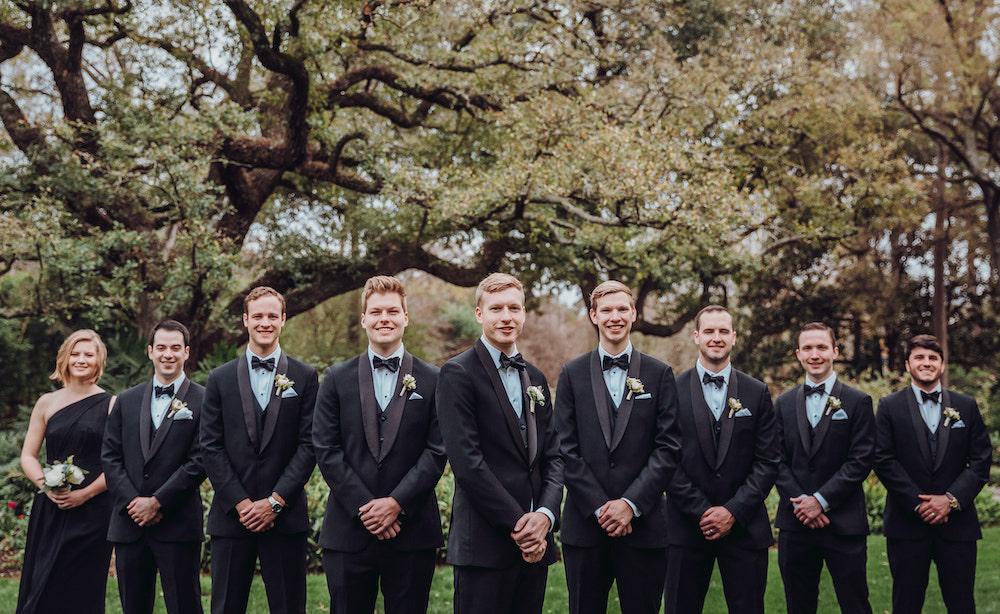 Groom poses with his wedding party, all dressed elegantly in black. 