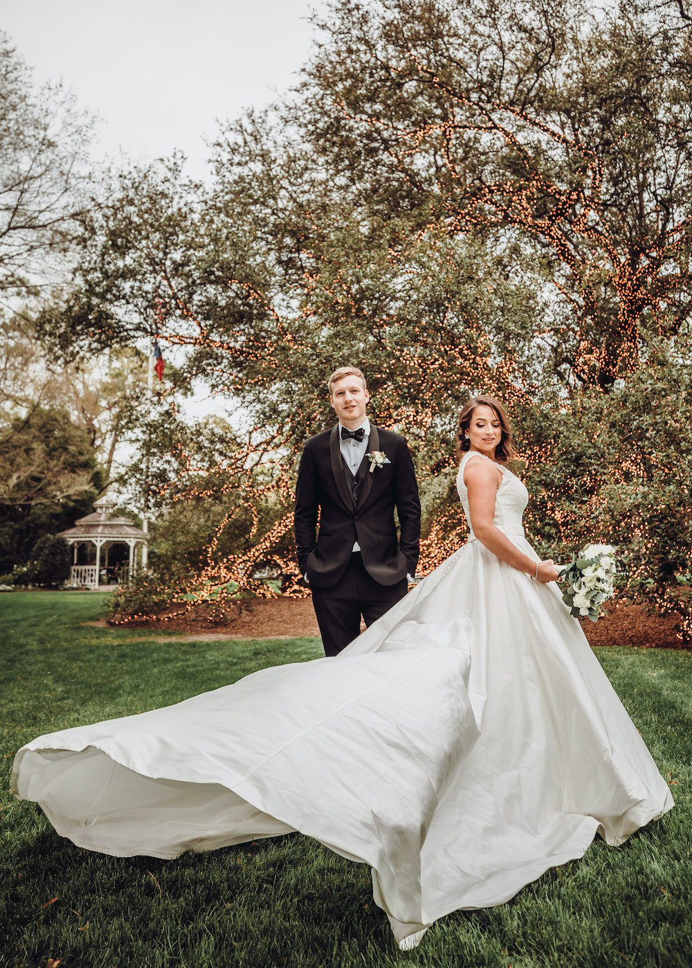 Bride wearing an elegant wedding gown and groom in black tuxedo posed in front of The Houstonian live oak tree