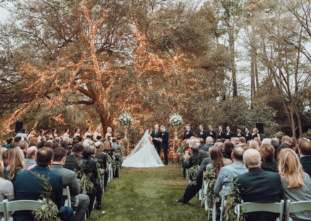 Bride and groom during their wedding ceremony with guests watching at The Houstonian Hotel, Club & Spa in front of gorgeous sparkling live oak tree. 