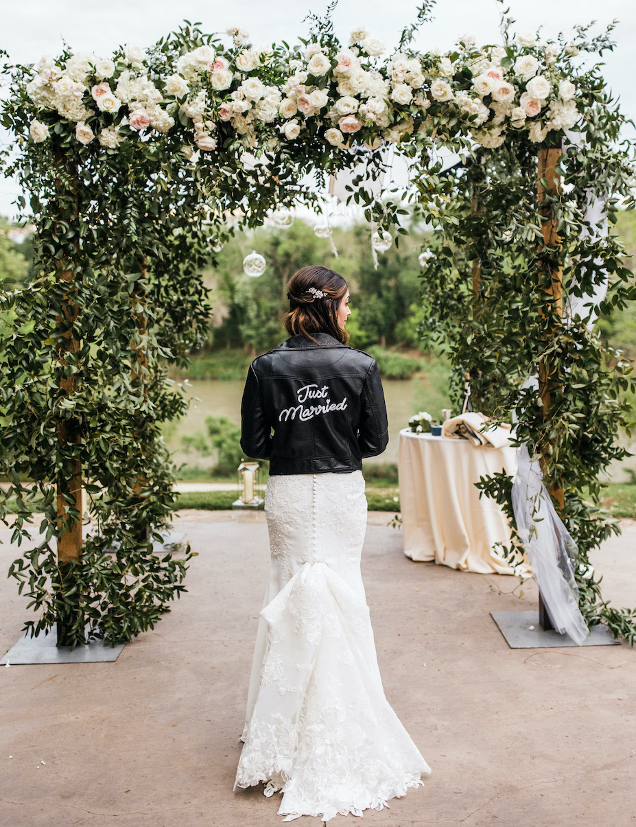 Bride posing with a black leather jacket that reads "just married" over white lace wedding gown. 