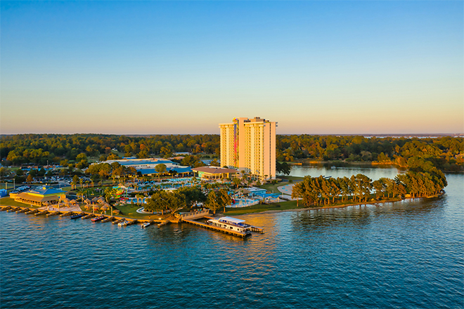 The Margaritaville Lake Resort, Lake Conroe stands tall on the waterfront, surrounded by trees and blue water.