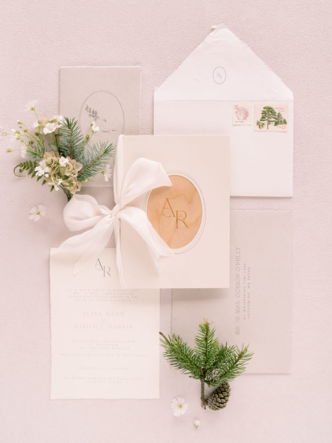 Minimalist wedding invitation with pops of natural wood and spruce sprig and floral boutonnière.