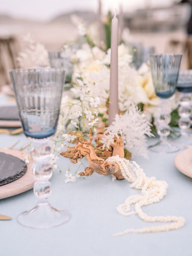 Blue glassware, candles, and driftwood elements accent white flowers on this wedding tablescape on Cannon Beach in Oregon.