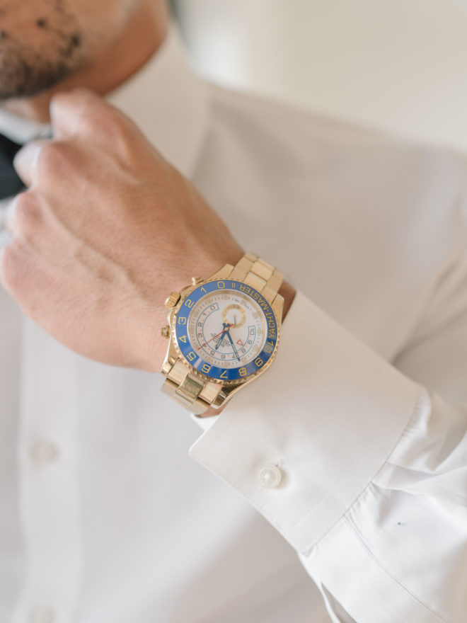 Groom adjusting black bow tie wearing gold wrist watch with a blue and white face and gold numbering. 