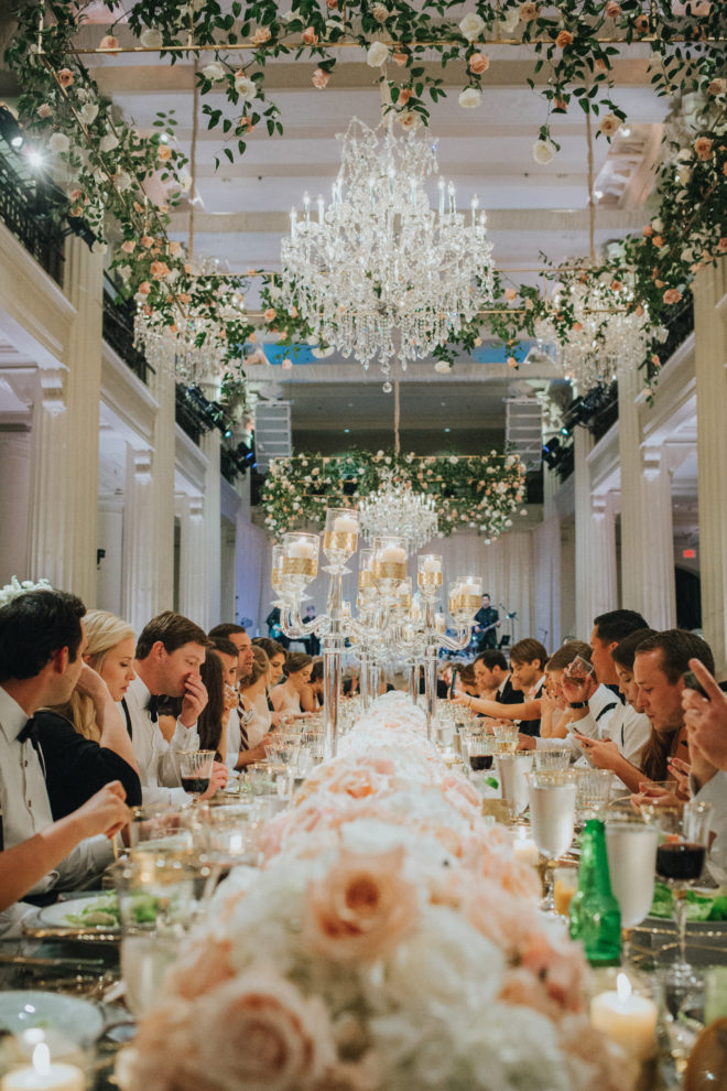 A wedding tablescape at the Corinthian Houston features pink and white flowers and happy guests dining. 