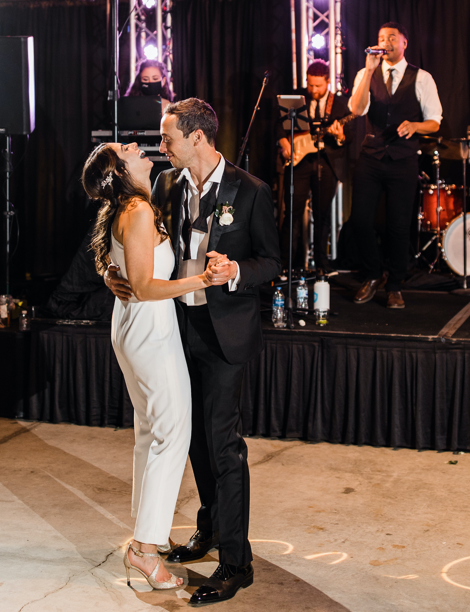 Bride and groom share an intimate last dance in their empty venue. The bride is wearing a one shoulder white jumpsuit that she changed into for the end of the celebrations.