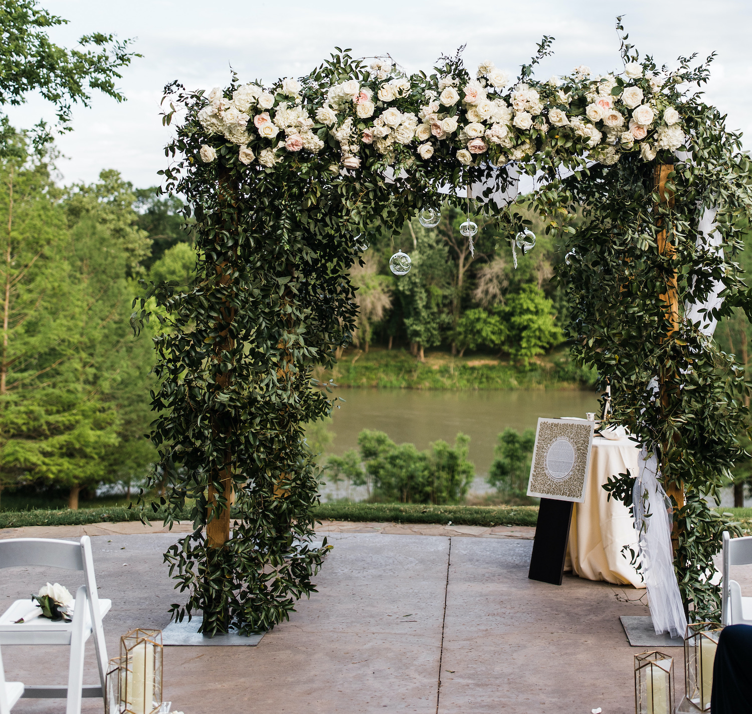 Greenery covered chuppah with mother's veil tied in the front right post in front of the late mother of the bride's reserved chair and personal bouquet.