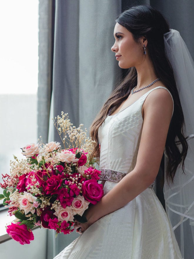 Bride in white princess gown with long brunette hair and mid length veil looks out the window at Hyatt Regency Houston Hotel. 
