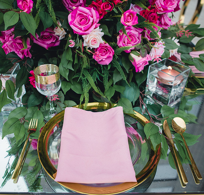 Vibrant, city chic wedding flowers in bright pink and blush flow across the table accenting gold glassware, dishware, and flatware.