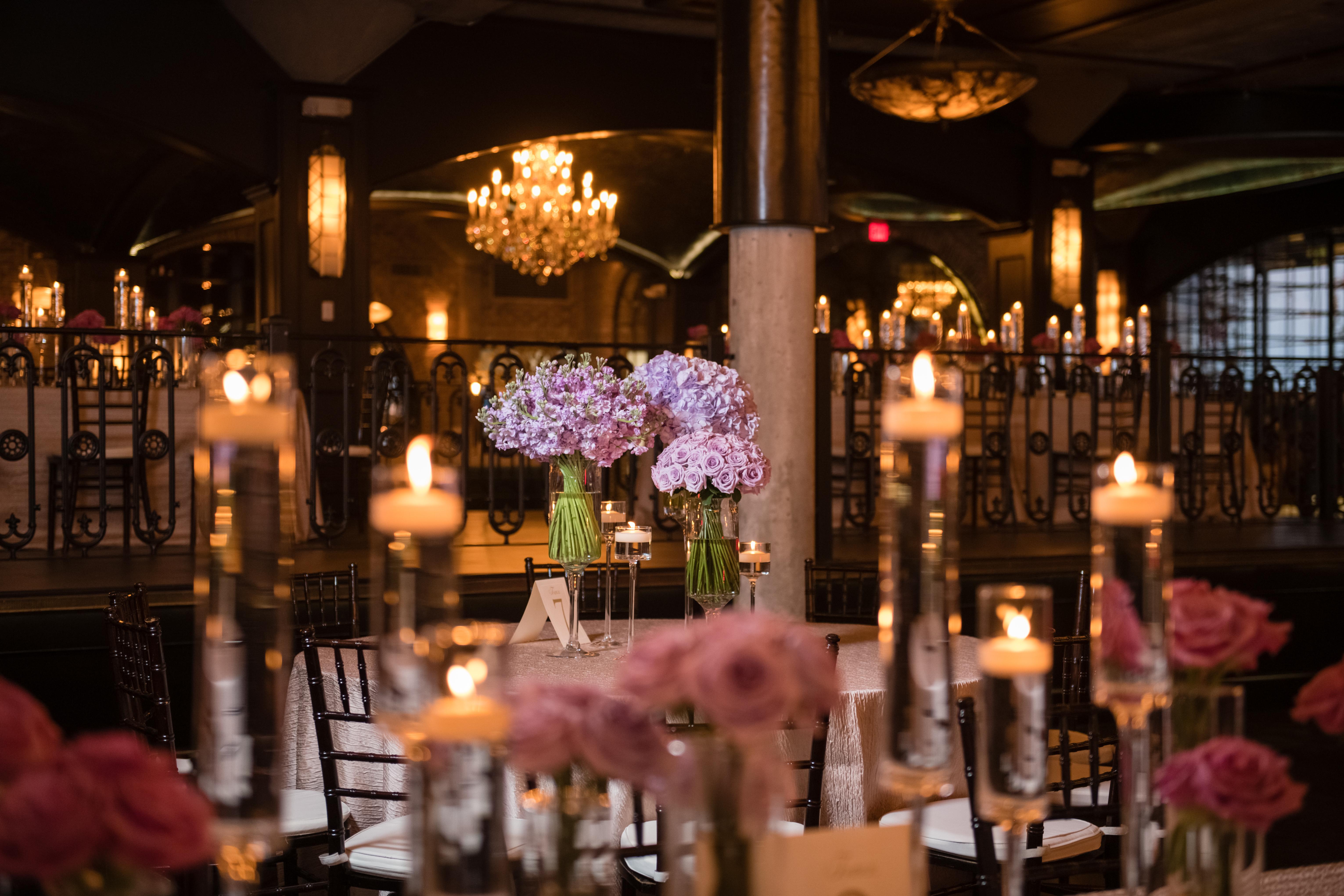 Long tables are lined with centerpiece vases of purple flowers and candles.