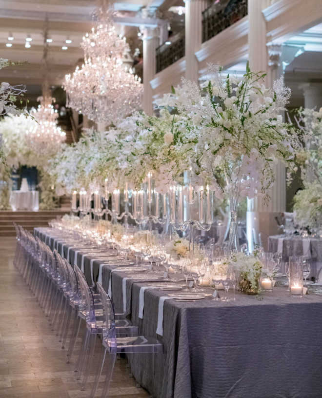 Long tablescape with tall white blooming floral centerpieces and lit candles inside the interior of Corinithian Houston. 