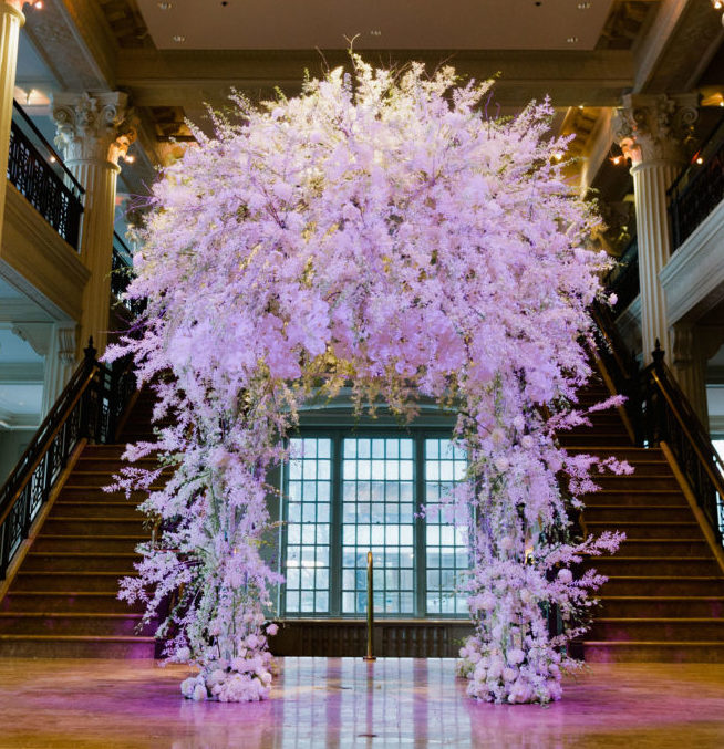 Soft lavender wisteria adorn an arch flanked by two stairs inside the historic houston venue, Corinthian Houston.