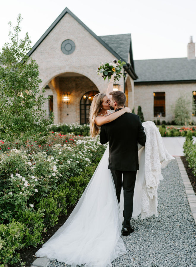 Groom carrying and kissing bride in front of Iron Manor.