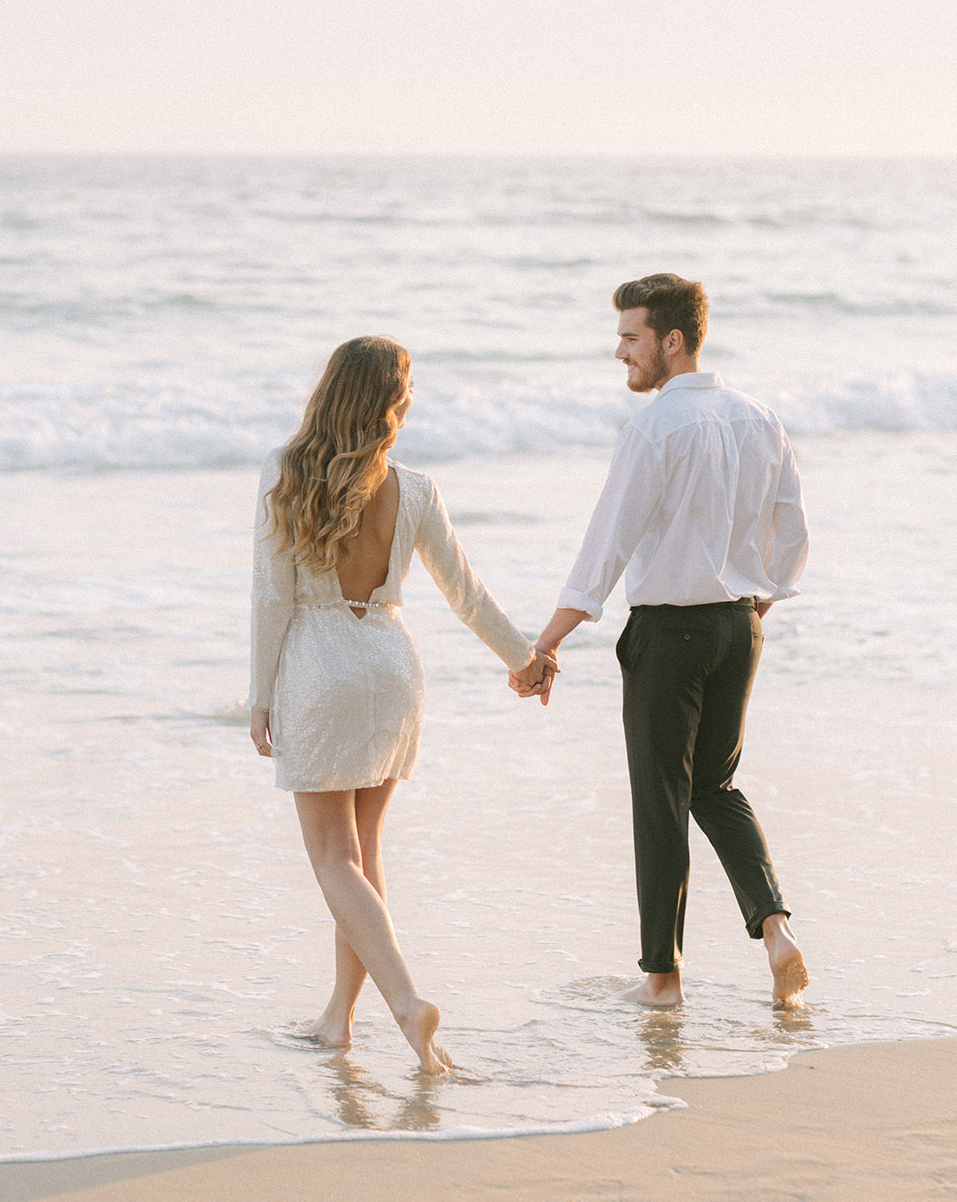 The bride and groom walk hand in hand towards the ocean during this beach elopement wedding styled shoot.