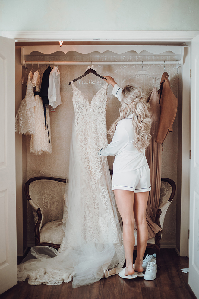 A bride reaches for her wedding dress on a hanger in the closet as she prepares to put it on.