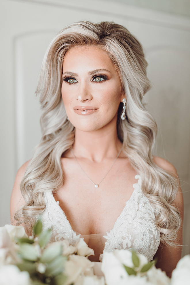 A portrait of the brides neutral smoky eye, full lashes, and nude lipstick paired with full, perfect curls and dangling diamond earrings. 
