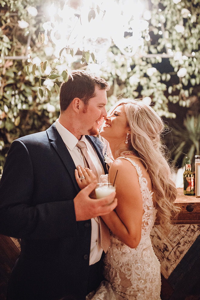 A bride and groom smile at eachother while sharing a drink and silly moment during their wedding reception.