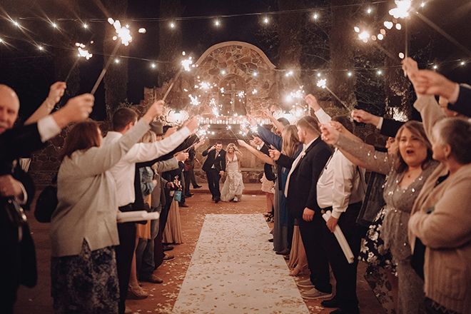 The bride and groom begin their exit from their Madera Estates wedding as their guests hold sparklers up above.
