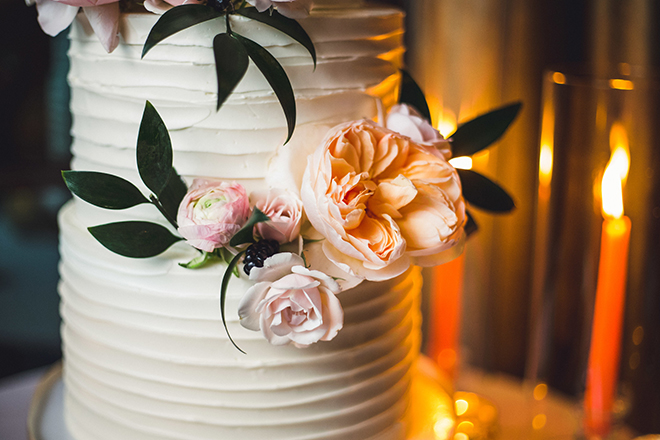 A spatula-iced white cake with peach and blush flowers and blueberries in a close-up shot of the floral details.