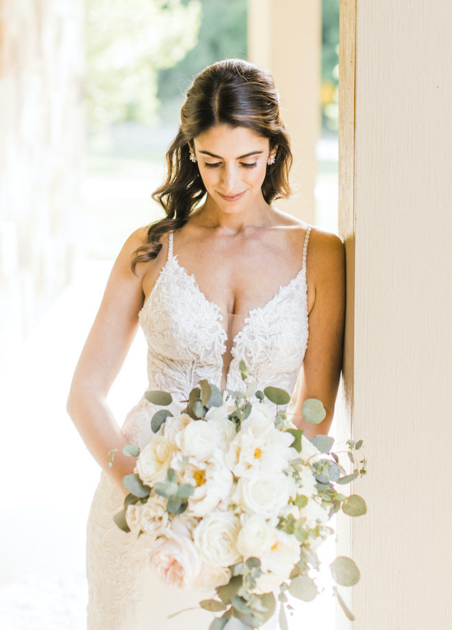 Bride, with hair pulled back in half updo wearing strappy beaded white bridal gown, standing against a pillar outside a suite at the Hyatt Lost Pines Resort and Spa. 