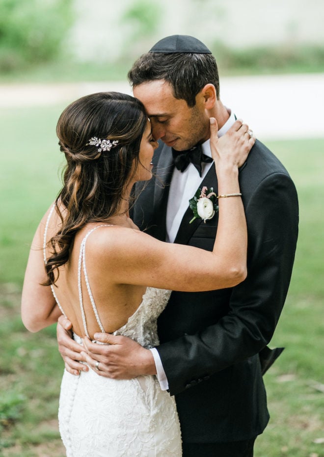 Groom, wearing wedding band, holding bride, in long white beaded wedding gown, beside a river at Hyatt Lost Pines Resort. 