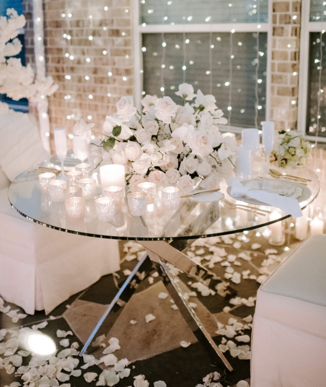 Small glass table set with white mercury glass votives, fresh white roses and scattered white rose petals for an intimate elopement ceremony by Plants N Petals. 