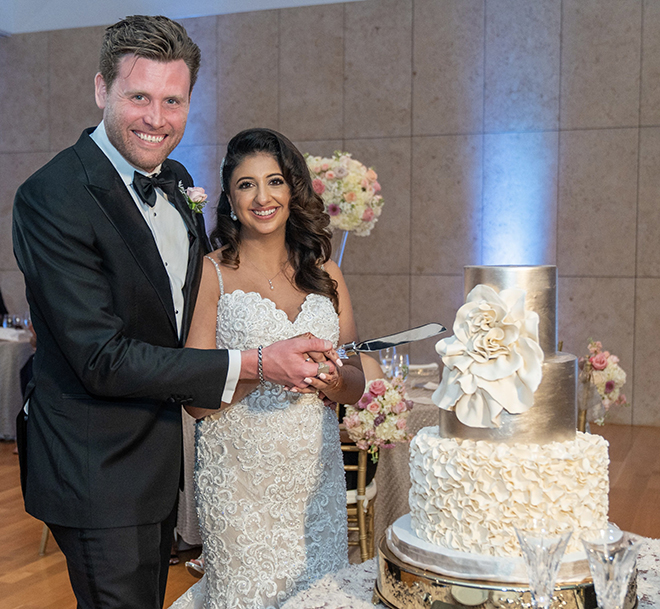 A newlywed couple cuts into their three-tiered white and gold floral-adorned cake by Common Bond Bistro & Bakery.