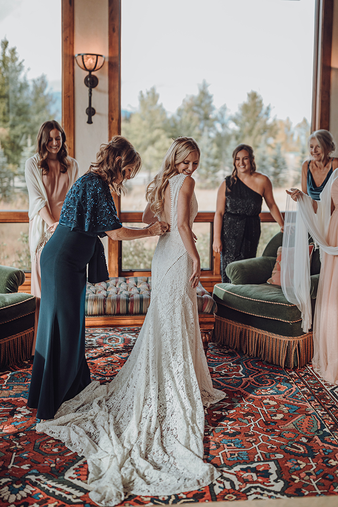 The mother of the bride finishes buttoning her daughter's wedding dress before her fall wedding.