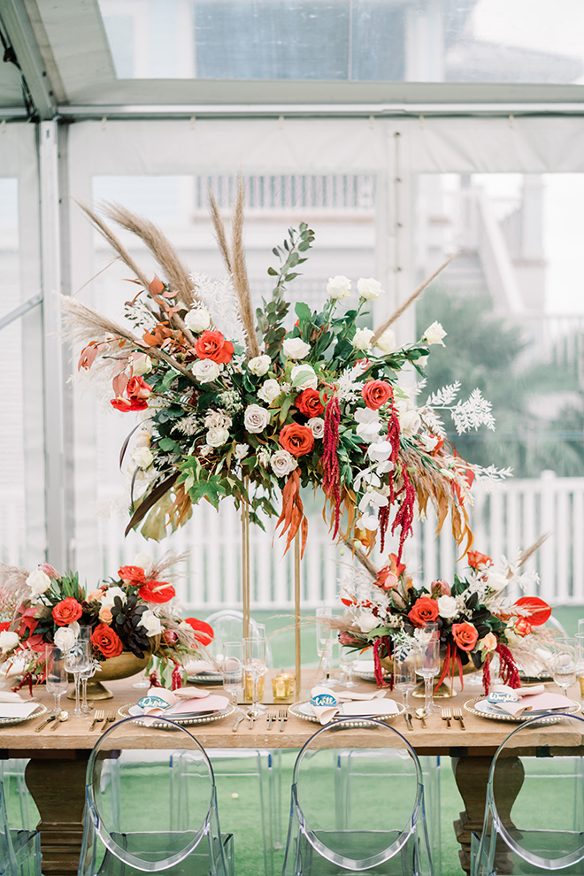 The sunset colored wedding palette pops with cascading floral arrangements of orange, red, and blush flowers with long sprigs of tan pampas grass.