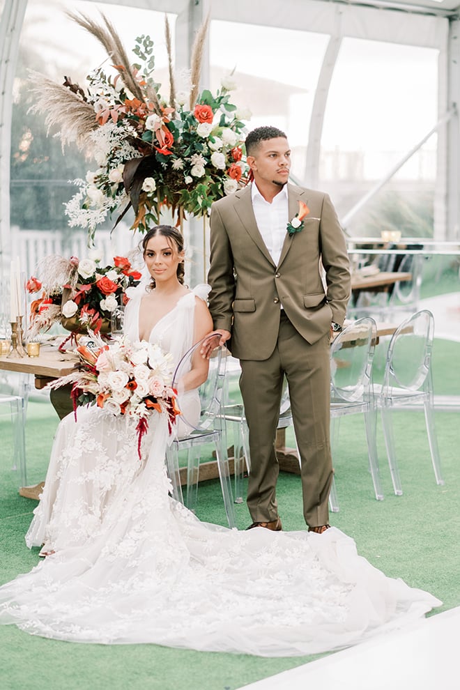 A beautiful bride in a Galia Lahav dress holds her vibrant bouquet while sitting next to her groom in a taupe suit.