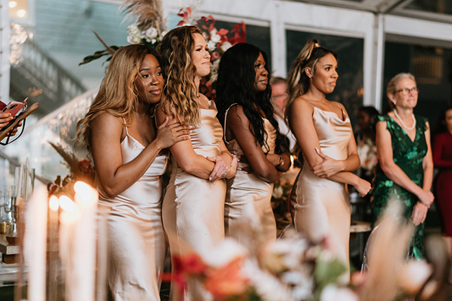 Bridesmaids in champagne midi dresses watch as their friend exchanges vows with her groom.