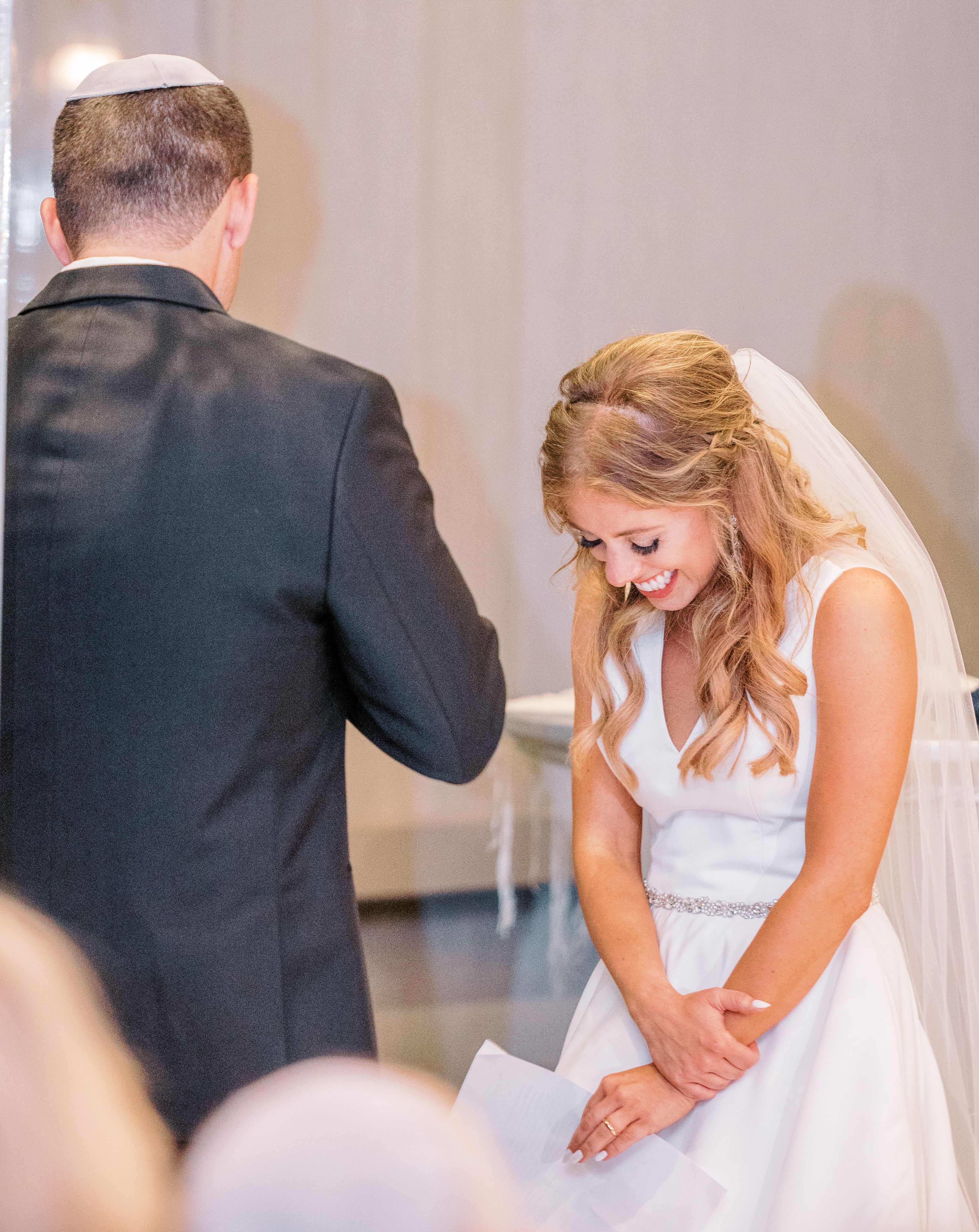 Bride smiling down as groom says his vows.