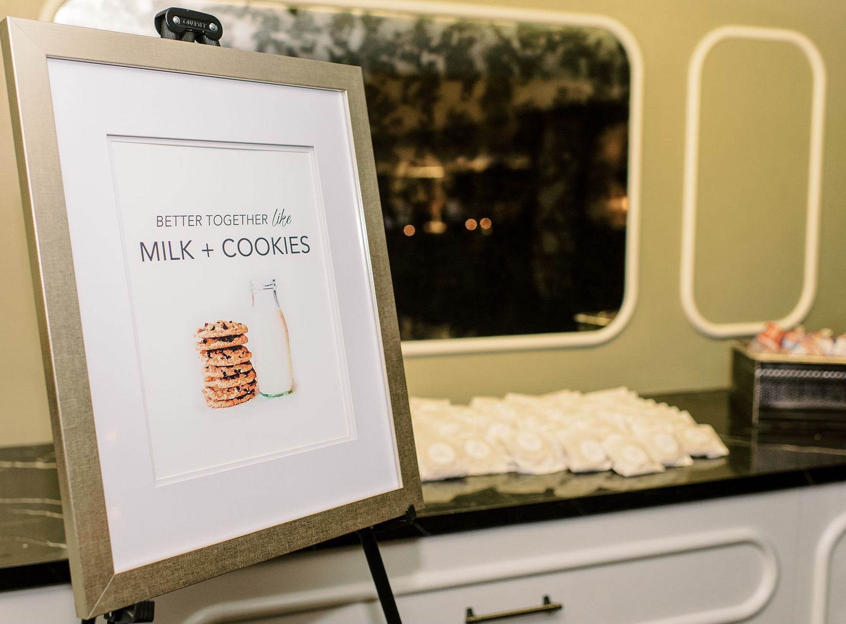 A milk and cookies sign stands in front of a table with warm cookies and milk for the wedding guests.