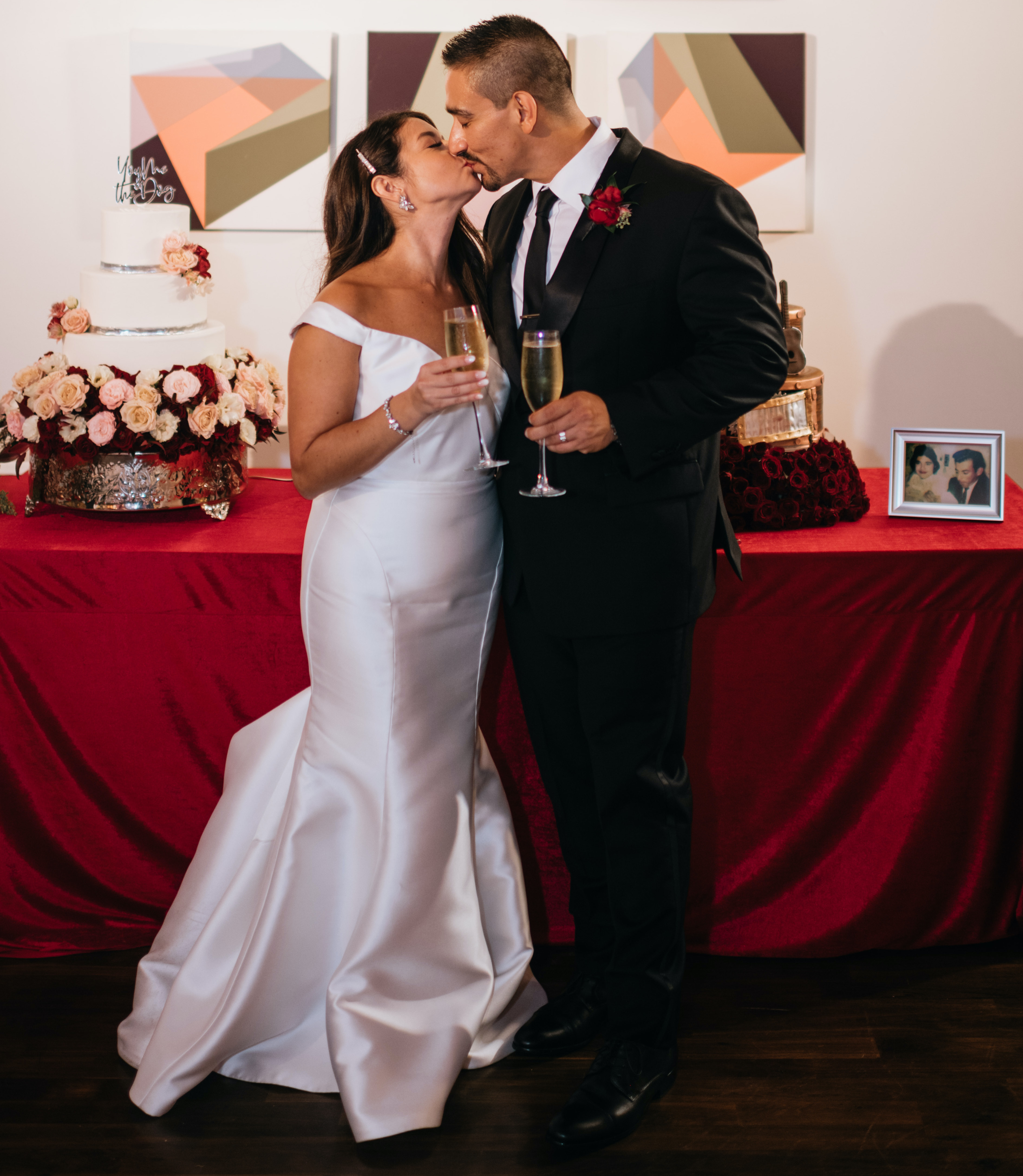 The bride and groom hold champagne as they kiss in front of their wedding cakes.